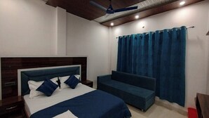 A bedroom with a bed, a nightstand, a blue sofa, and a ceiling fan. - Hotel RISHI (Bhatwari)