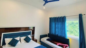 A bedroom with a large bed, a smaller bed, a ceiling fan, and a window with curtains. - Hotel RISHI (Bhatwari)