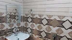 A bathroom with a wooden vanity, a sink, a mirror, and a patterned tile wall. - Hotel RISHI (Bhatwari)