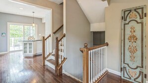 A spacious interior with a wooden staircase, a kitchen area, and a large window providing natural light. - South Side home with garage, game room, gym & deck near downtown, stadiums and Carson Street (Pittsburgh)