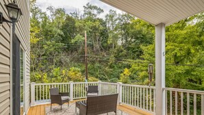 A covered outdoor deck with a white railing, two wicker chairs, and a patterned rug. - South Side home with garage, game room, gym & deck near downtown, stadiums and Carson Street (Pittsburgh)