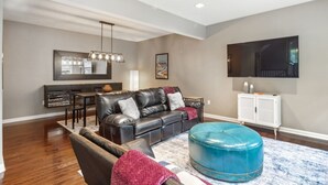 A living room with a leather sofa, ottoman, and a flat-screen TV mounted on the wall. - South Side home with garage, game room, gym & deck near downtown, stadiums and Carson Street (Pittsburgh)