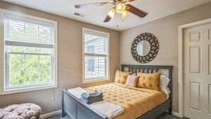 A bedroom with a bed, two windows, a ceiling fan, a mirror, and a door. - South Side home with garage, game room, gym & deck near downtown, stadiums and Carson Street (Pittsburgh)