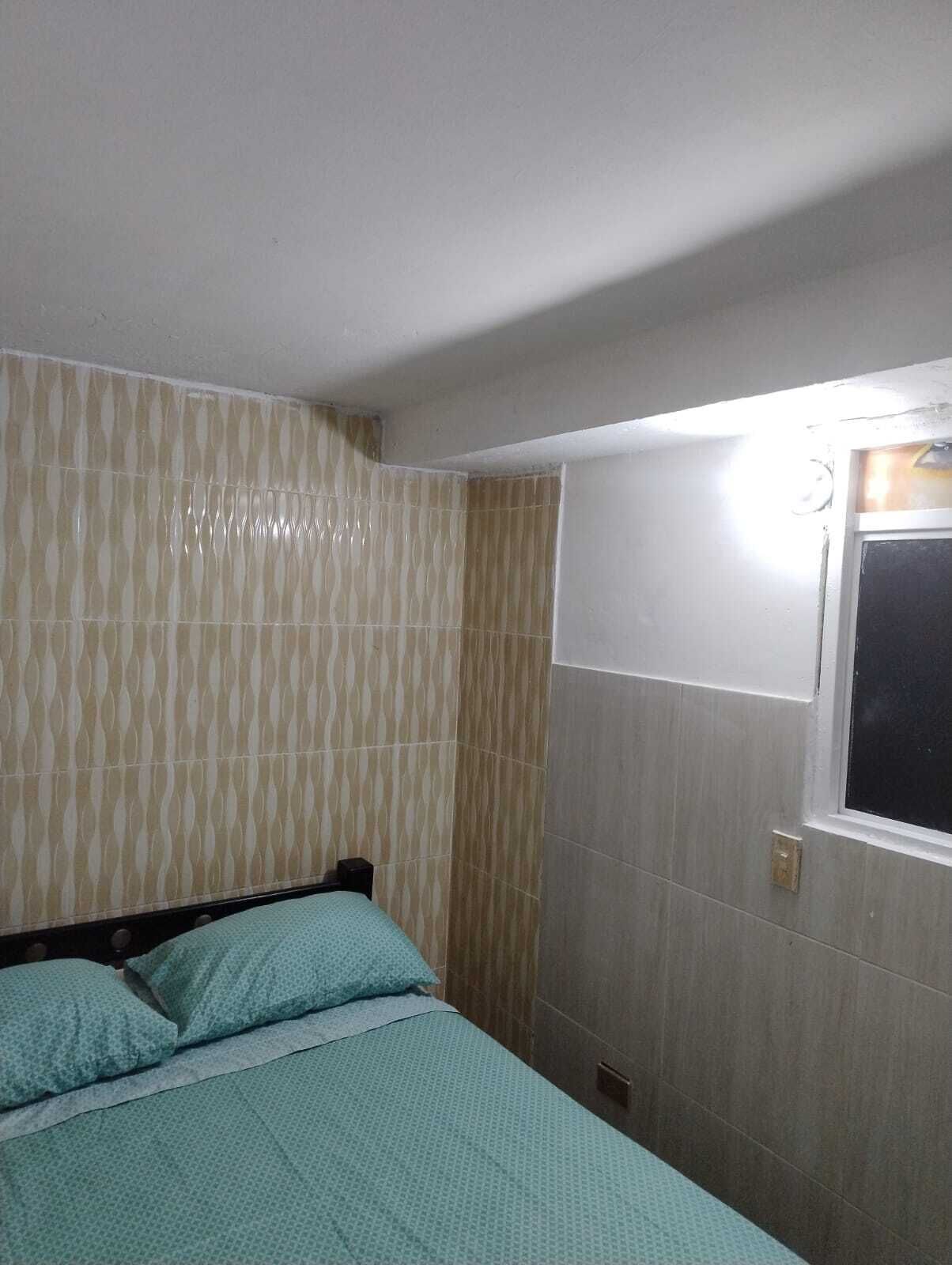 A bedroom with a bed, patterned wallpaper, and a window with a light fixture.