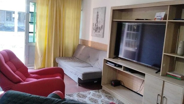 A living room with a sofa, a red armchair, a television on a wooden stand, and a yellow curtain. - Apartment Iwoo HR with WiFi, AC in welcoming Villavicencio (Villavicencio)
