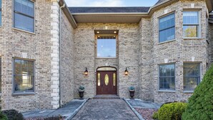 A two-story brick house with a central entrance, two side entrances, and a covered front porch. - Elegant Home w/7BRs, Game Room, Luxury Yard, Pool (Chester)