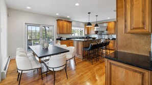 A modern kitchen with wooden cabinets, a central island, and a dining area with white chairs. - Elegant Home w/7BRs, Game Room, Luxury Yard, Pool (Chester)