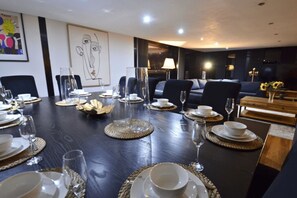 Ein Essbereich mit einem dunklen Holztisch, der für eine Mahlzeit gedeckt ist, umgeben von Stühlen und einer Couch.