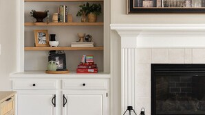 Una sala de estar con chimenea, muebles blancos y un cuadro con una vista urbana.