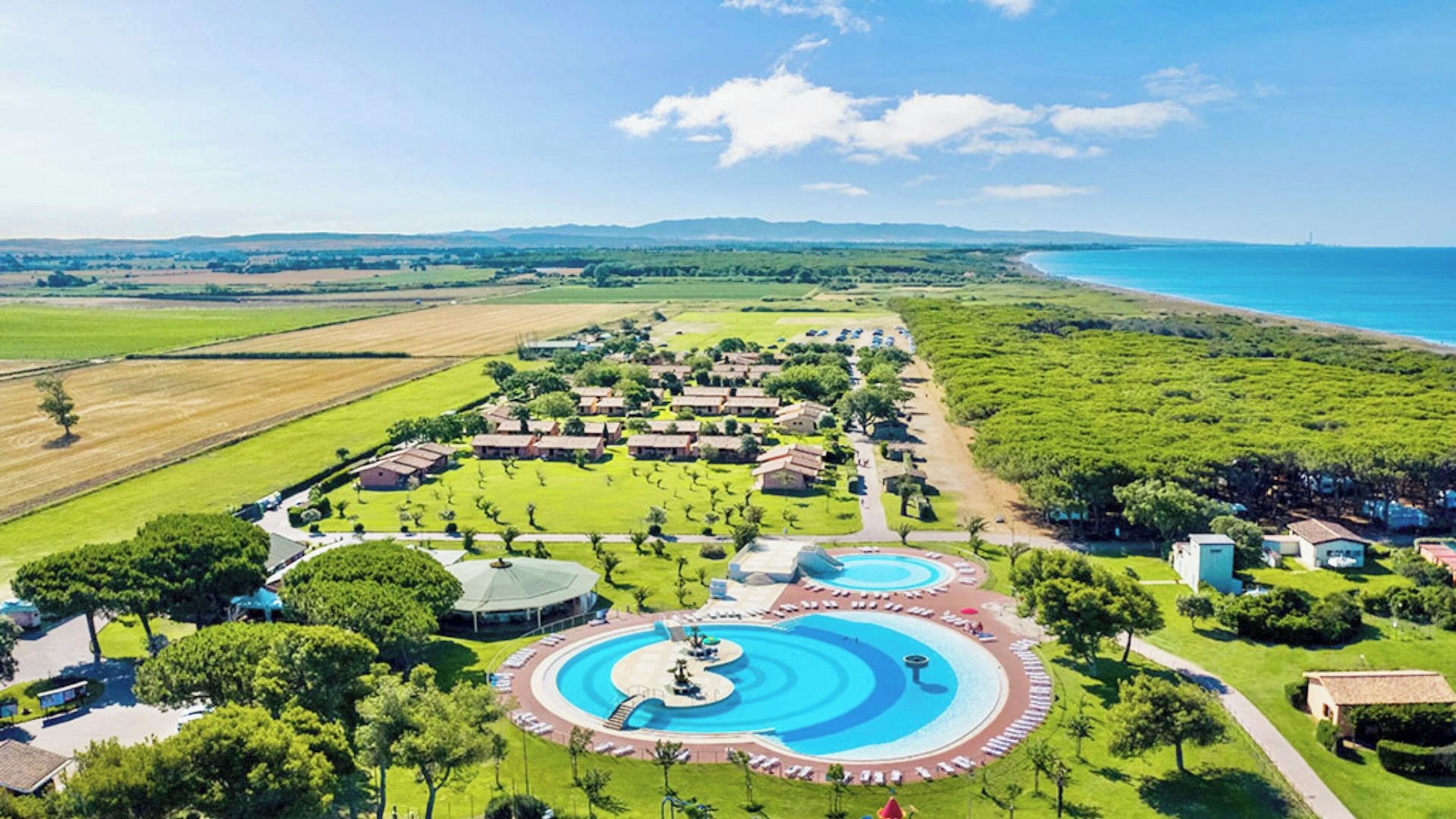 Vista aérea de un complejo turístico con varias piscinas, villas y una playa.