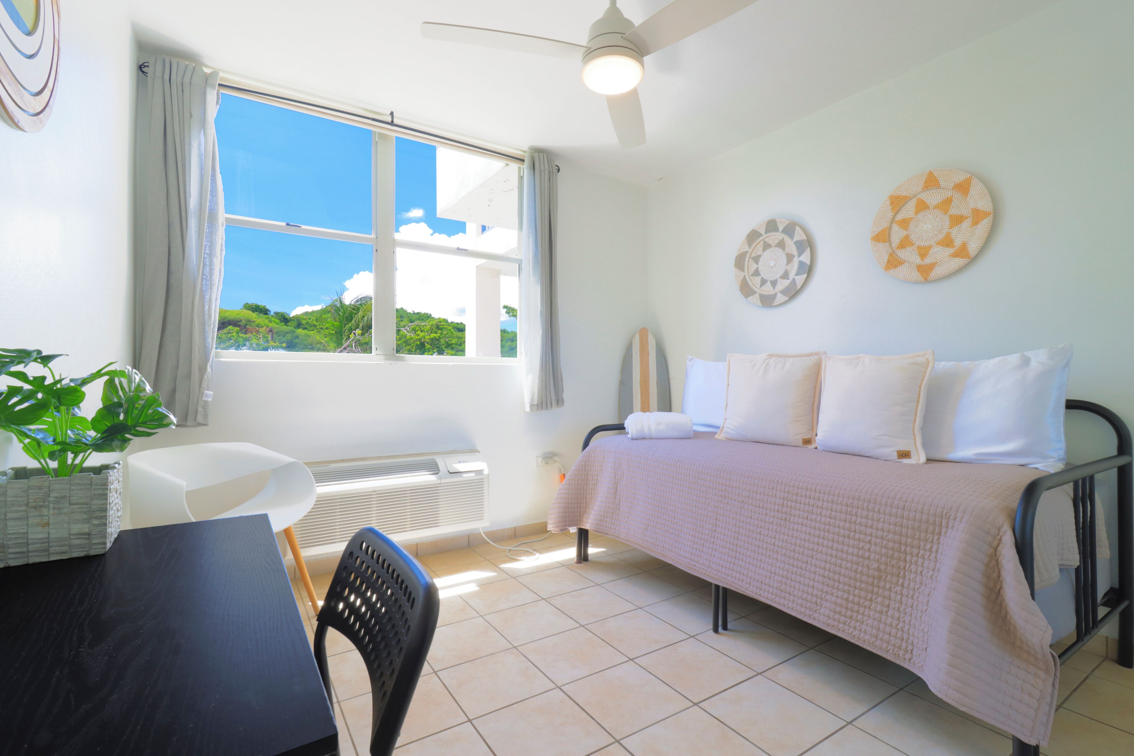 Un dormitorio con cama, escritorio, silla, ventana con cortinas y ventilador de techo.