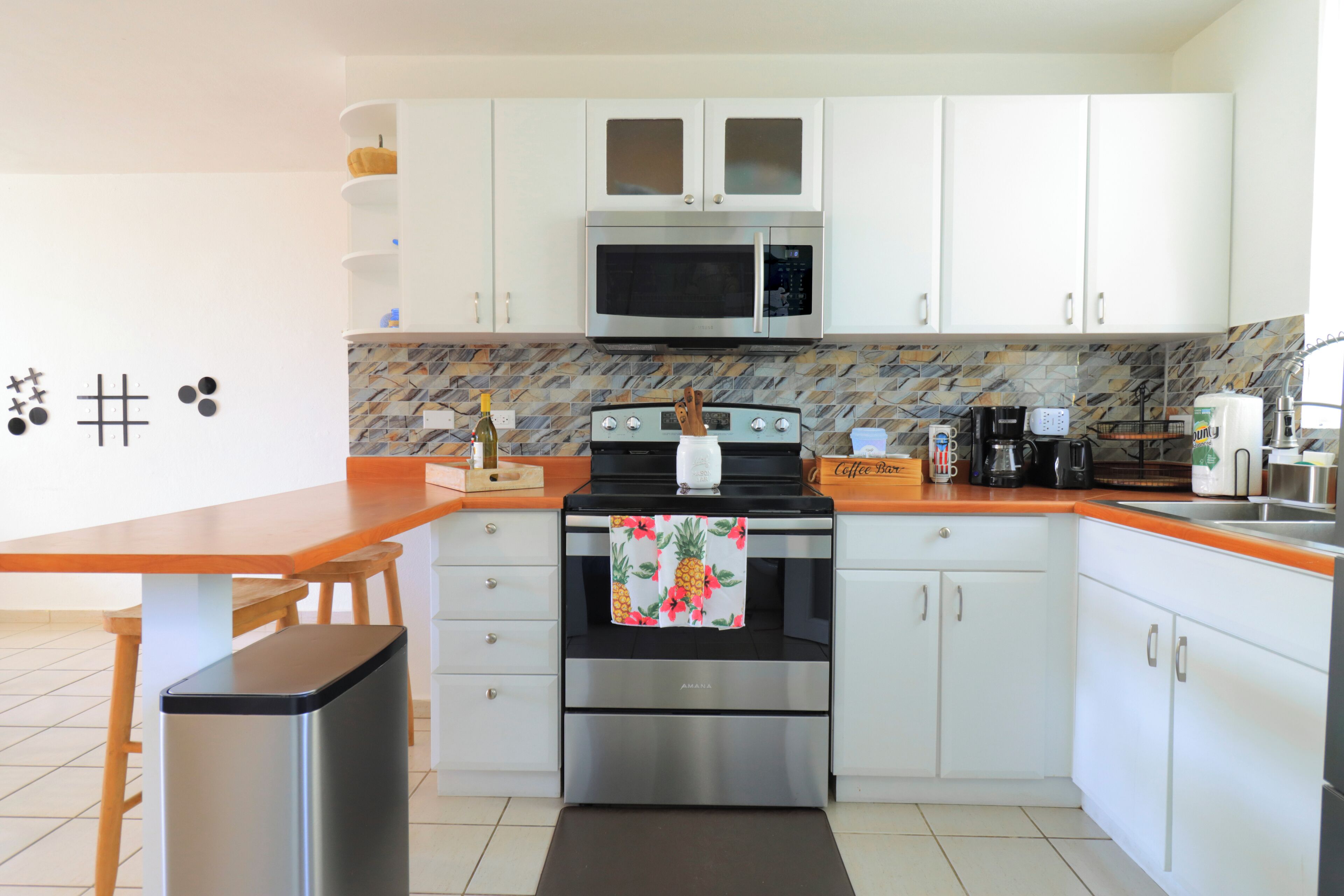A modern kitchen with white cabinets, a microwave, an oven, and a coffee station.