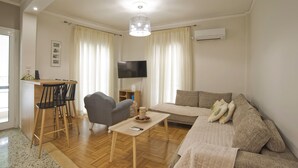 A living room with a sofa, a coffee table, a TV, and a dining area with chairs and a table. - Fabi's Place Luxurious 2BR, Fully Renovated Apt (Kipseli)