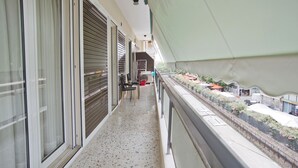 A balcony with a view of a street, a small table with chairs, and a red bucket. - Fabi's Place Luxurious 2BR, Fully Renovated Apt (Kipseli)