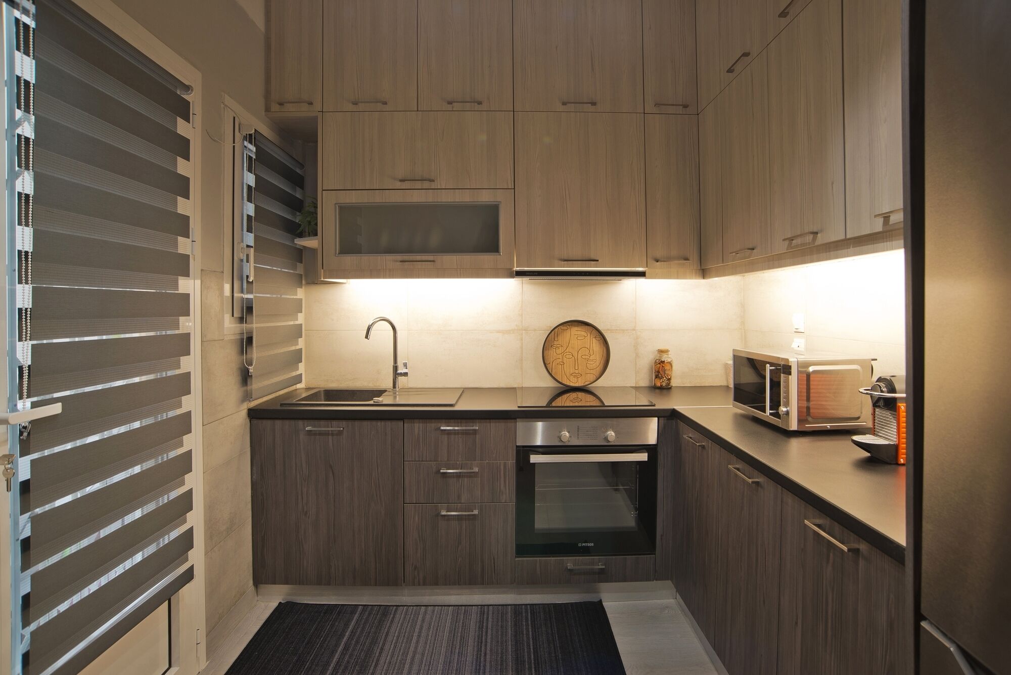 Une cuisine moderne avec des meubles en bois, un évier en acier inoxydable, un four encastré et un four à micro-ondes.