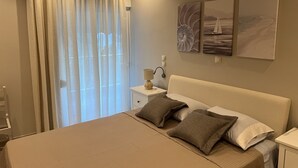 A neatly arranged bedroom with a large bed, a bedside table with a lamp, and three wall-mounted artworks. - SeaNfinity Spotless, 1BR Apt with Beach View (Nea Palatia)