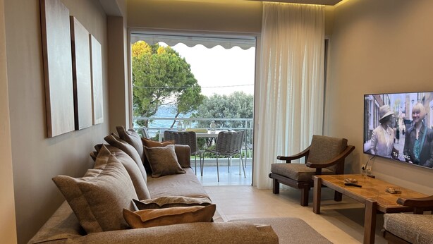 A modern living room with a sofa, chairs, a coffee table, and a TV. - SeaNfinity Spotless, 1BR Apt with Beach View (Nea Palatia)