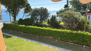 A well-maintained garden with a neatly trimmed hedge, a paved pathway, and a view of the sea. - SeaNfinity Spotless, 1BR Apt with Beach View (Nea Palatia)