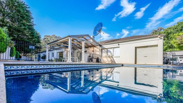 A swimming pool with a clear reflection, a covered area with columns, and a building with a garage door.