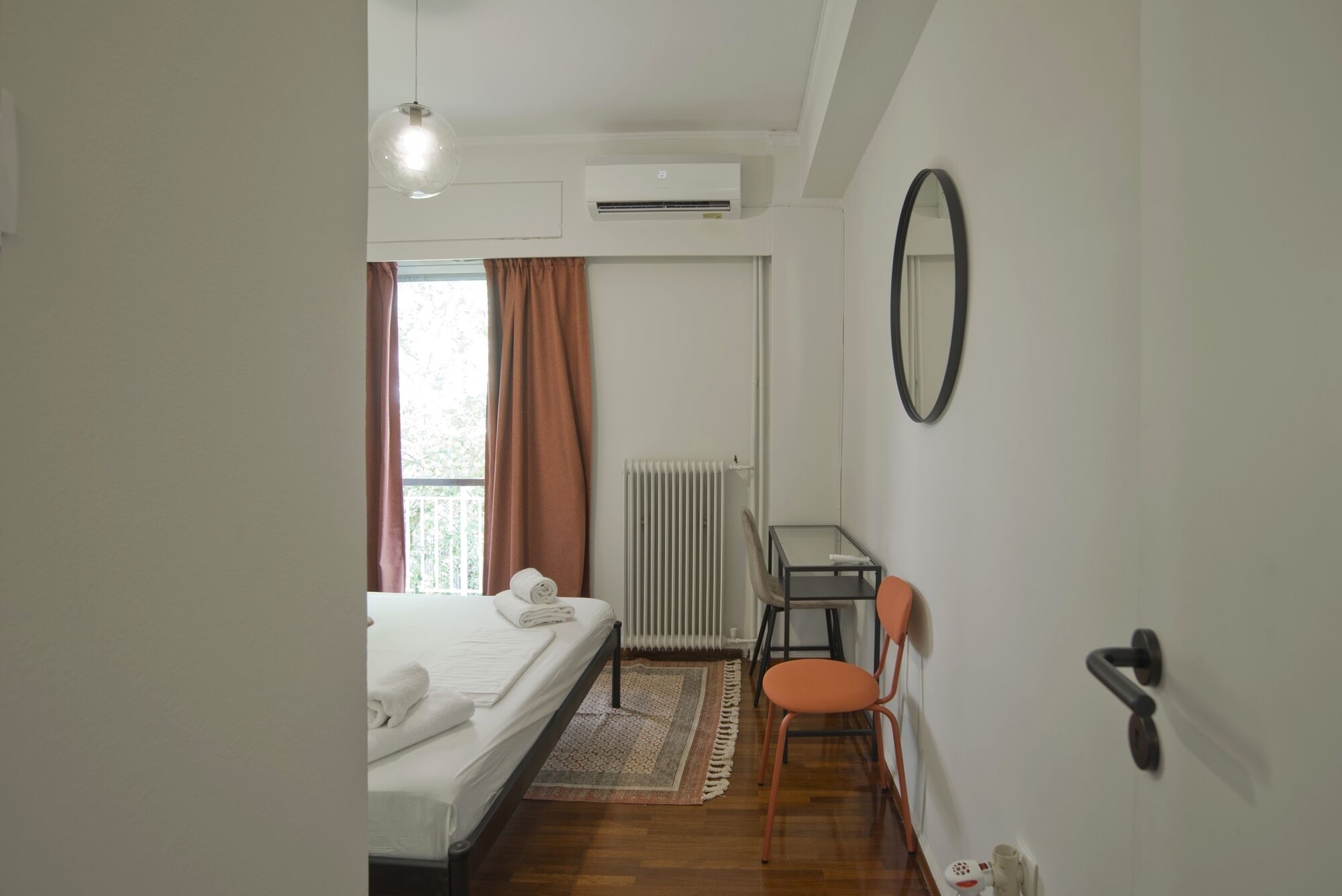 A bedroom with a bed, a radiator, a desk, a chair, and a mirror.