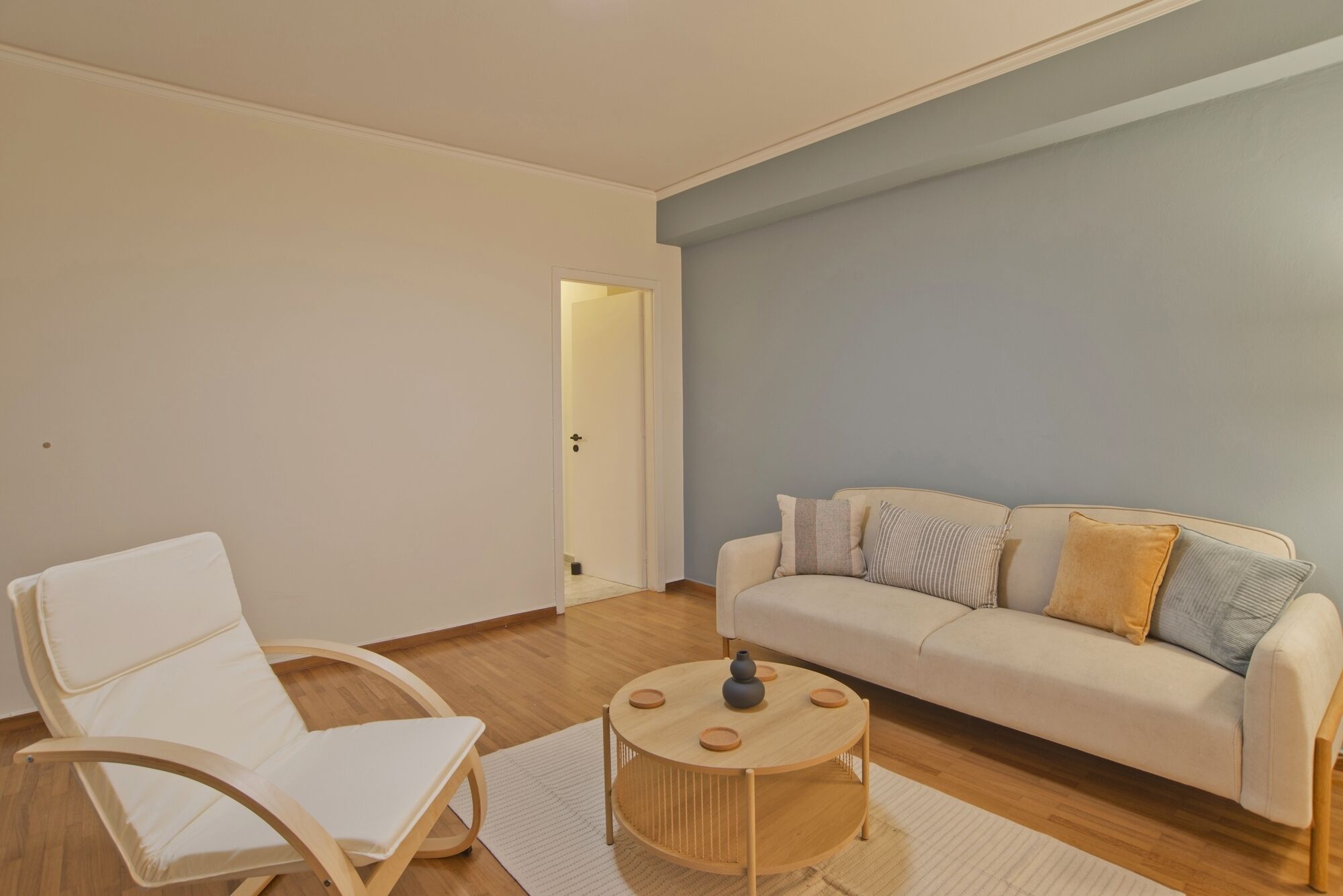 A living room with a white sofa, a white chair, and a round wooden coffee table.