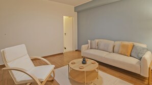 Una sala de estar con un sofá blanco, una silla blanca y una mesa de centro redonda de madera.