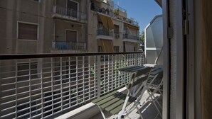 Un balcón con barandilla de metal, vista de un edificio de varios pisos con balcones y un cielo azul despejado.
