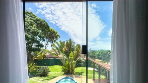 Vista attraverso una finestra con tende bianche, che mostra una piscina, un prato verde e alberi circostanti.