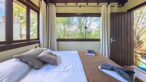 Una stanza con un letto, una testiera in legno, una finestra con tende e vista sugli alberi.