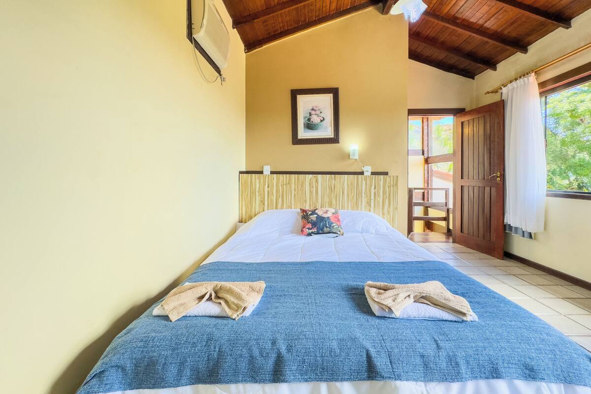 A hotel room with a wooden ceiling, a bed with a blue blanket, a wooden headboard, and a picture on the wall.