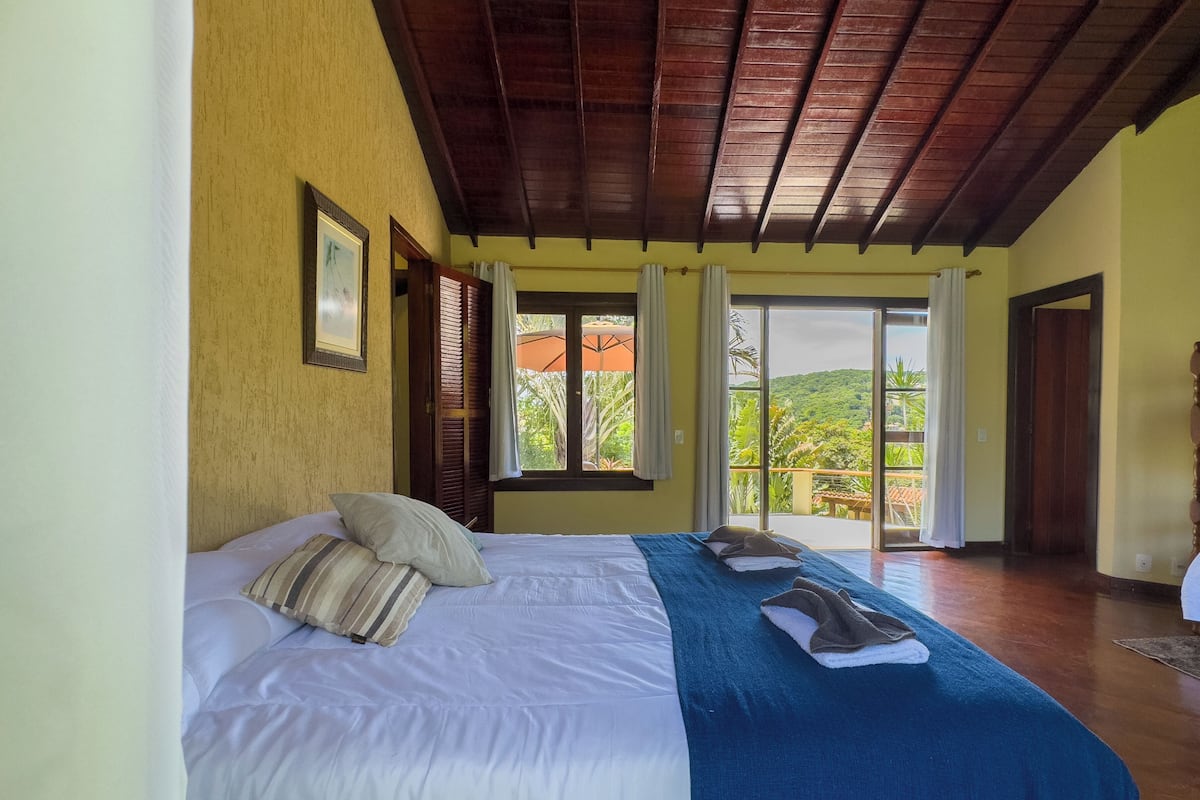 A bedroom with a bed, a blue blanket, and a view of greenery outside.