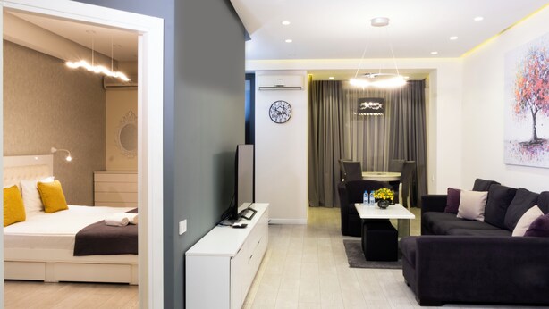 A modern hotel room with a bed, a desk, a sofa, and a dining area. - Welcome Northern Avenue Apartments (Yerevan)