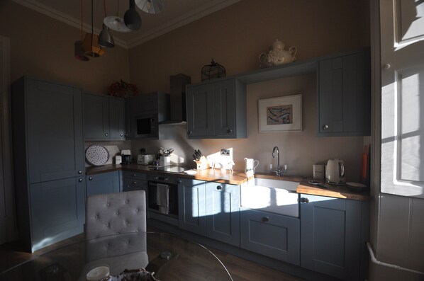 Una cocina con armarios azul claro, encimera de madera y diversos electrodomésticos.