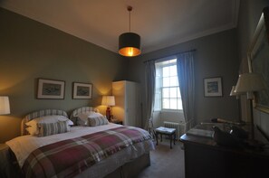 Een slaapkamer met een bed, nachtkastjes, een bureau, een stoel, een radiator en een raam met gordijnen.