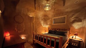 A cozy bedroom with a wooden bed, a nightstand, a wall-mounted lamp, and a decorative headboard.
