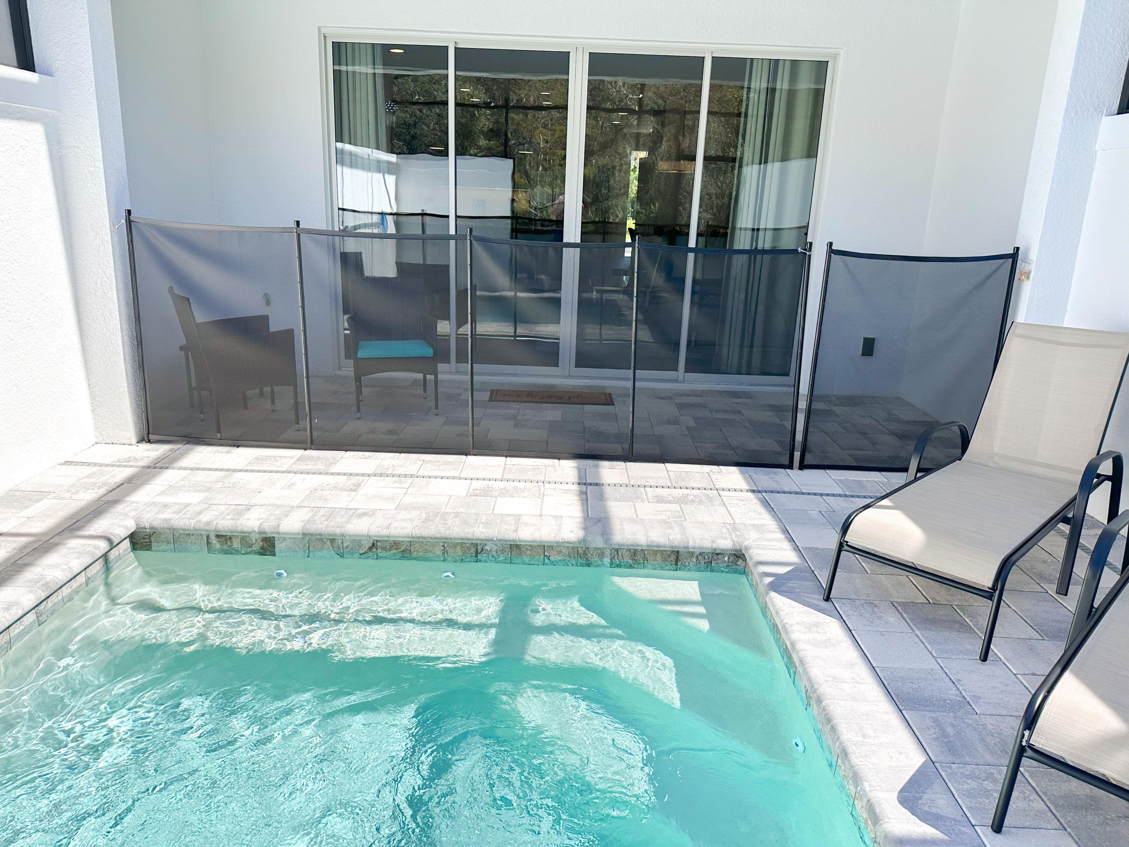 A swimming pool with a glass enclosure, a patio area with chairs, and a view of the outdoors.