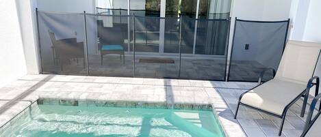 A swimming pool with a glass enclosure, a patio area with chairs, and a view of the outdoors.