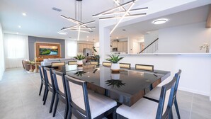 Uma zona de refeições moderna com uma mesa retangular grande, várias cadeiras e iluminação pendente.