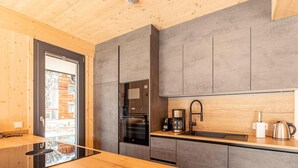 Una cuina moderna amb taula de fusta, forn de mur i cafetera.