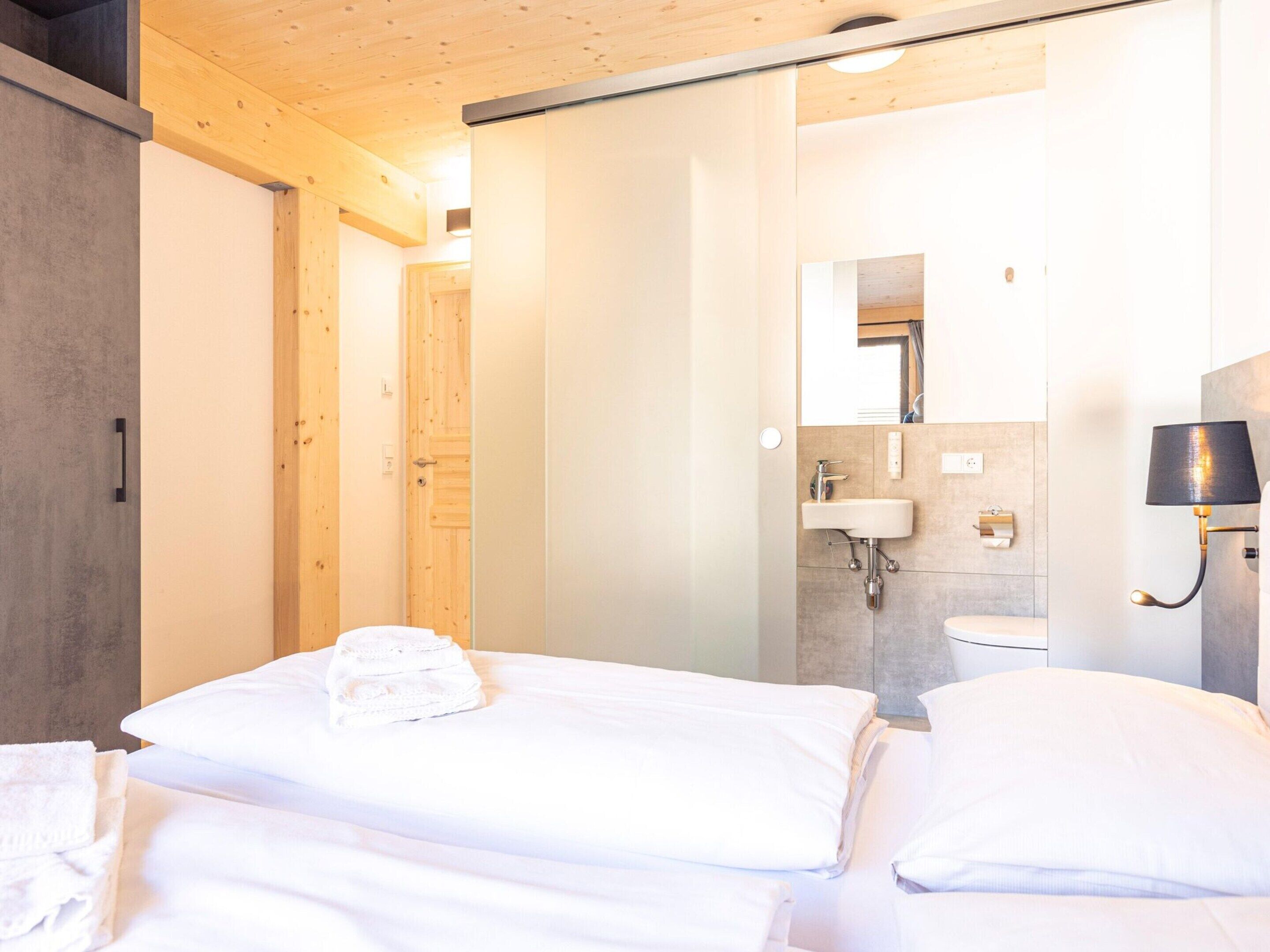 Et moderne hotelværelse med en stor seng, et badeværelse med håndvask og spejl, og trædetaljer.