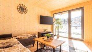 Un interior de fusta acollidor amb un sofà, una taula de centre, una televisió i vista a un paisatge nevàt a través d'una porta de vidre.