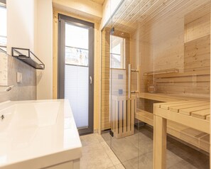 A modern bathroom with a large white sink, a glass shower enclosure, and wooden paneling. - Cosy Apartment With Sauna (Sankt Georgen am Kreischberg)