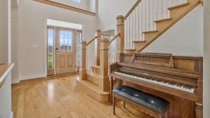 Um quarto espaçoso com um piano de cauda, escadaria de madeira e uma grande janela.
