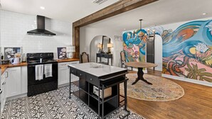 Una cocina moderna con una isla central, un comedor con mesa redonda y un mural llamativo en la pared.