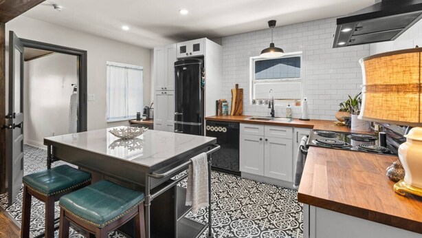 Una cocina moderna con una isla central, armarios blancos y un refrigerador negro.