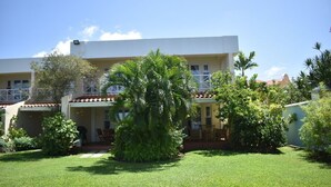 Un hotel con fachada blanca, varios balcones y un jardín bien cuidado con palmeras.