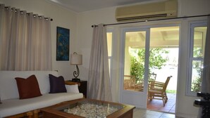 Una sala de estar con sofá, una mesa de centro de vidrio, lámpara y puerta corrediza de vidrio que da a un patio exterior.