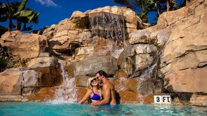 A couple in a pool with a waterfall and palm trees in the background. - 226 Spectrum new Loft 12 guests 5BDRS 15min Disney (Kissimmee)