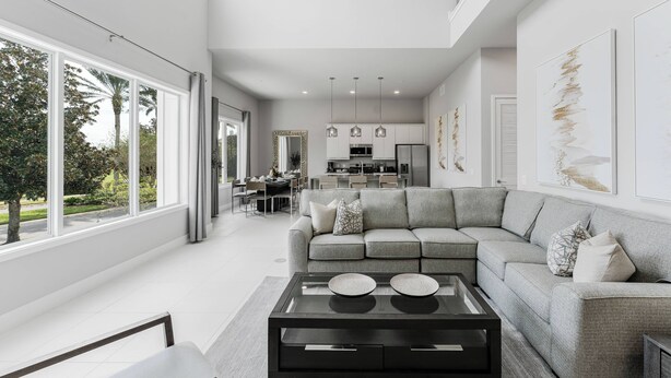 A modern living room with a grey sectional sofa, a glass coffee table, and large windows offering a view of the outdoors. - 226 Spectrum new Loft 12 guests 5BDRS 15min Disney (Kissimmee)