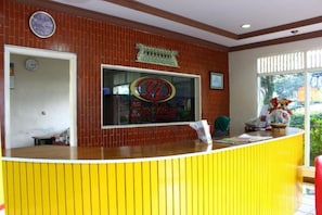 Un espace d’accueil avec un comptoir jaune, une horloge et une fenêtre donnant sur un paysage verdoyant.